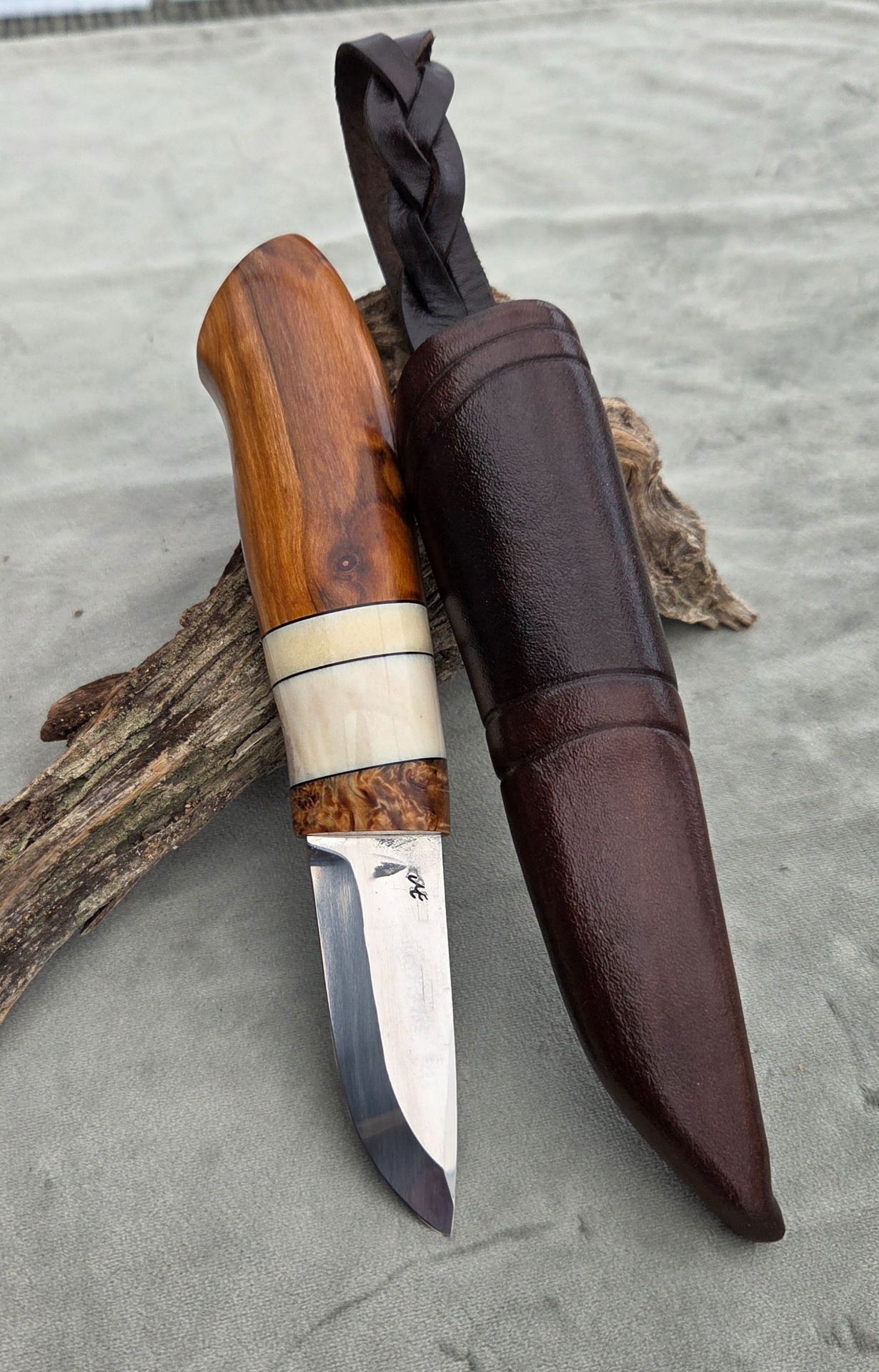 2026 "Glaskogen 3/2026". Rostfritt blad av Maikhel Eklund, Fat Bob. Skaft av äpple, front av stabiliserad masurbjörk. Detaljer av älghorn och vulkanfiber. Knivslida av färgat rårandsläder.